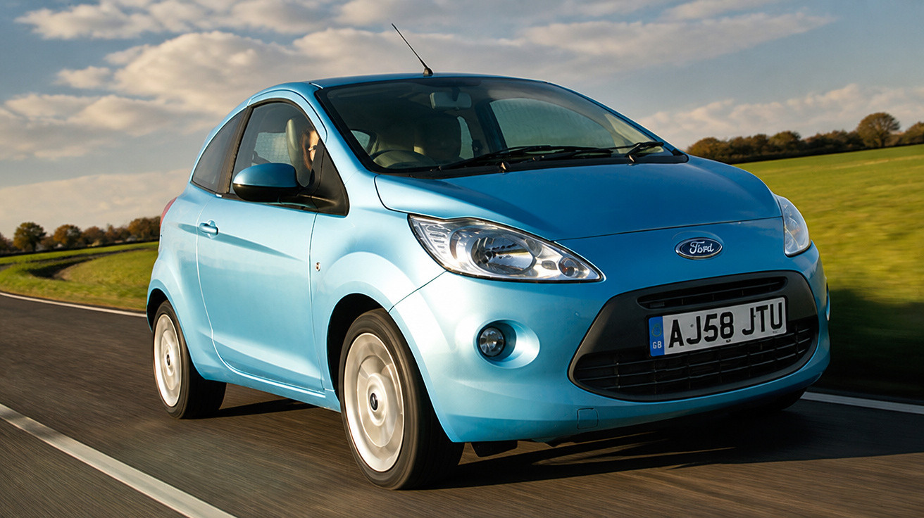 Carro azul compacto da Ford em movimento numa estrada rural com céu nublado ao fundo.