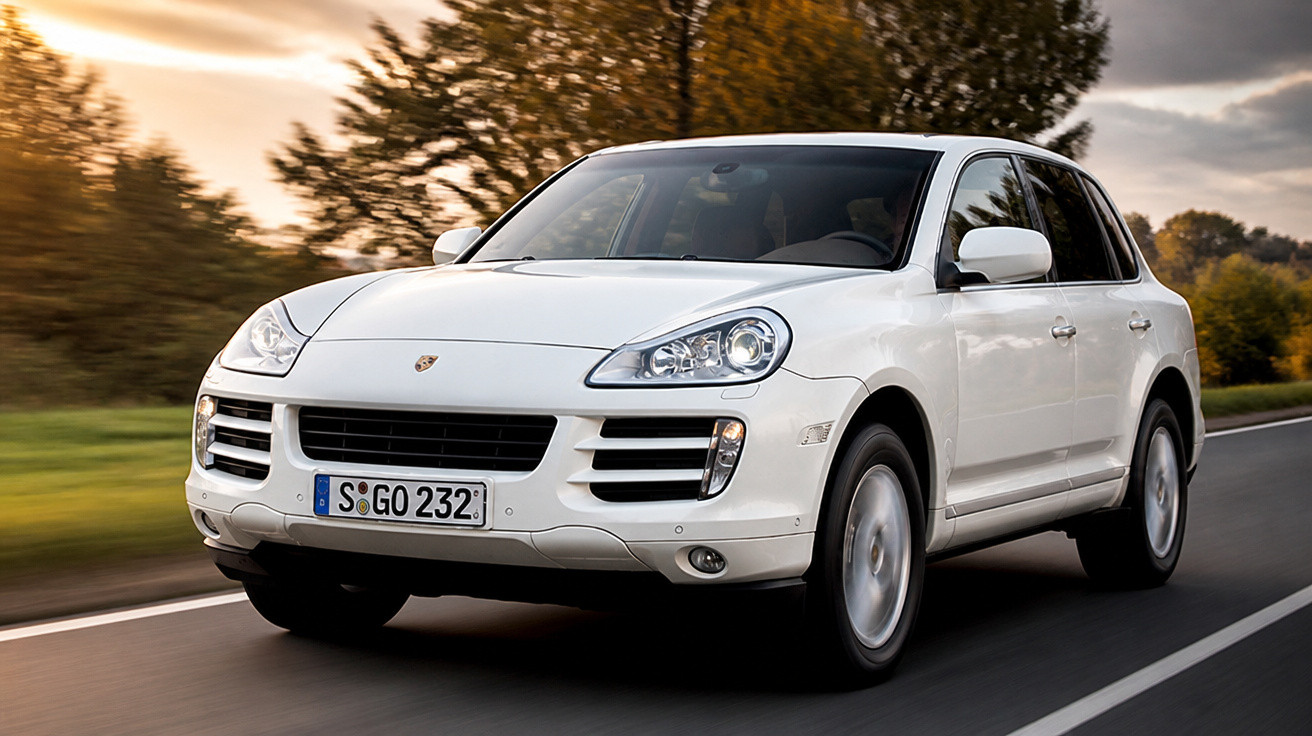 Carro SUV Porsche branco em movimento na estrada com árvores e céu ao fundo ao entardecer.