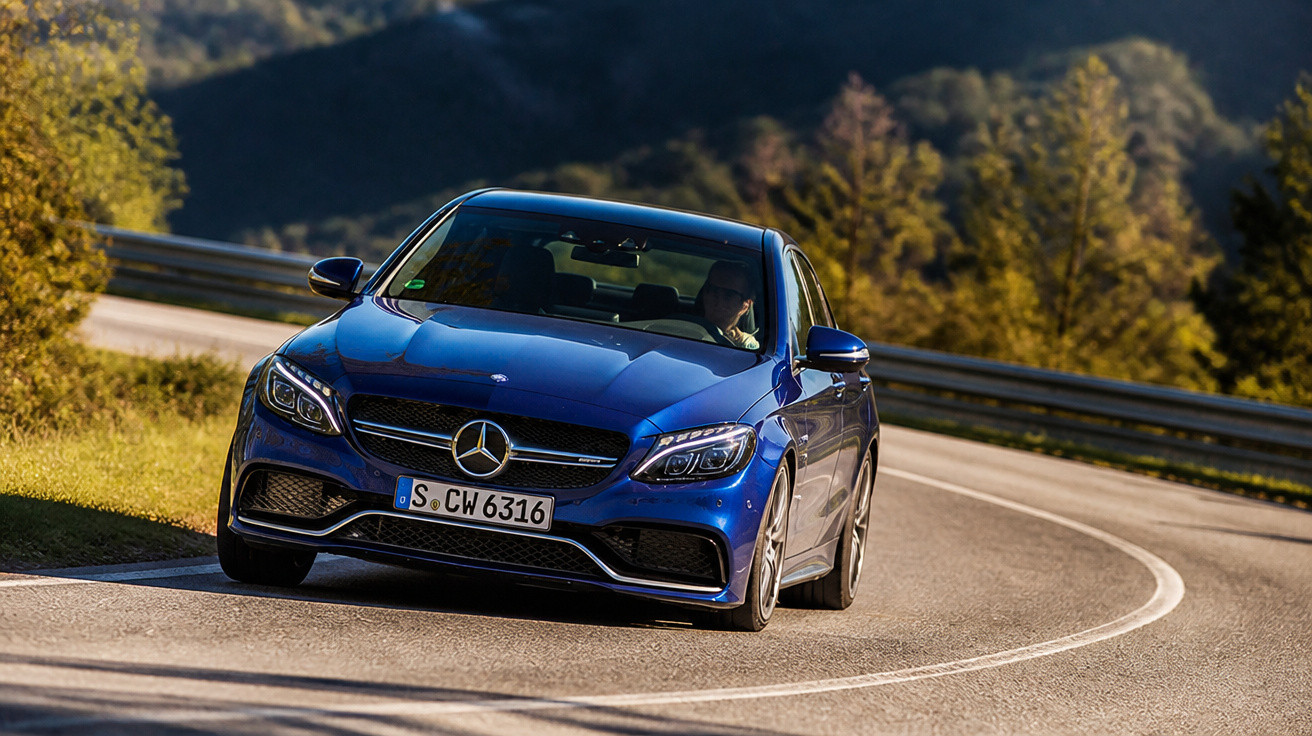Carro Mercedes-Benz azul em curva de estrada sinuosa com vegetação e montanhas ao fundo.