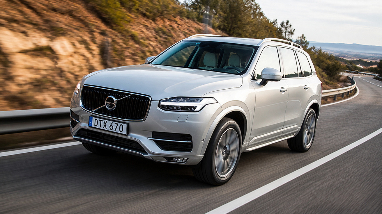 Carro SUV Volvo prata dirigido em estrada sinuosa com vegetação e montanhas ao fundo.