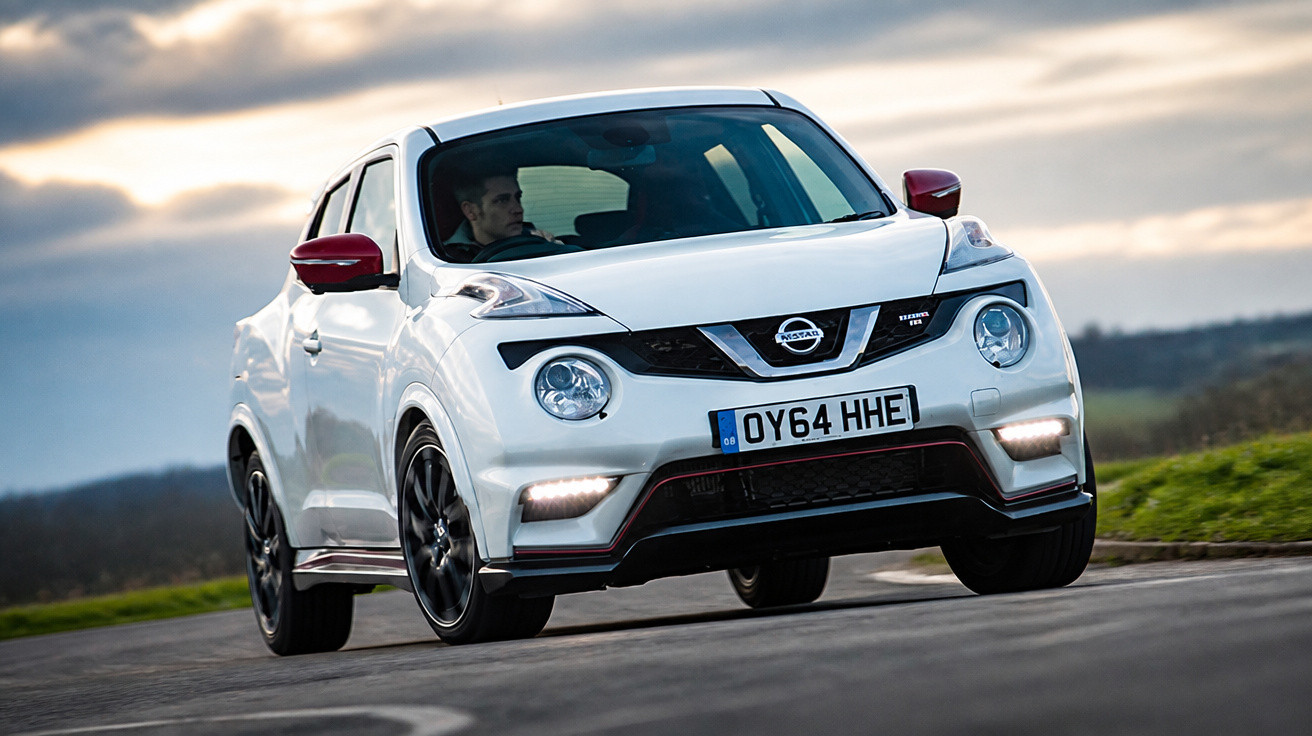 Carro branco Nissan Juke em estrada curva com motorista, céu nublado ao fundo.