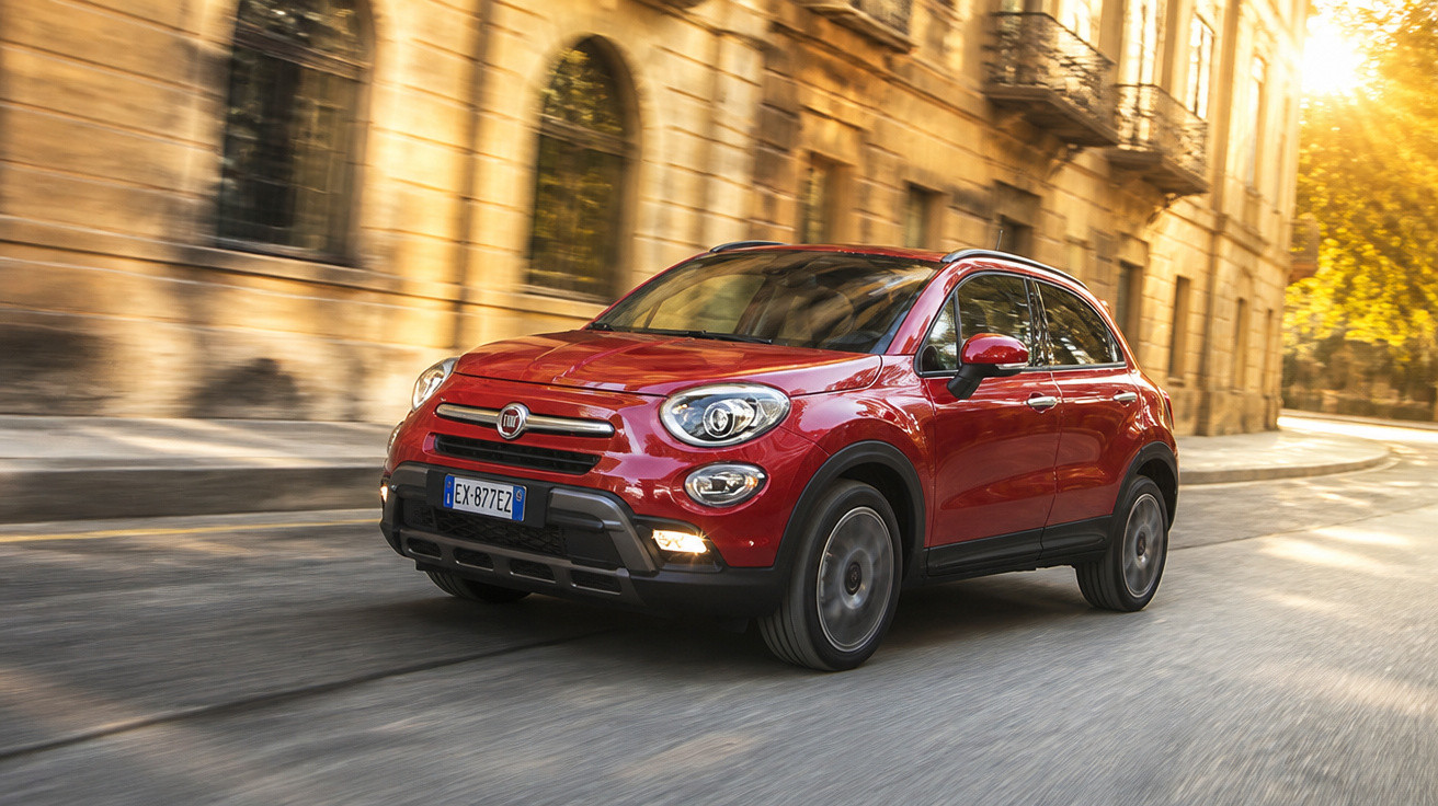 Carro SUV Fiat 500X vermelho transitando em rua com prédios históricos ao fundo com luz do pôr do sol.