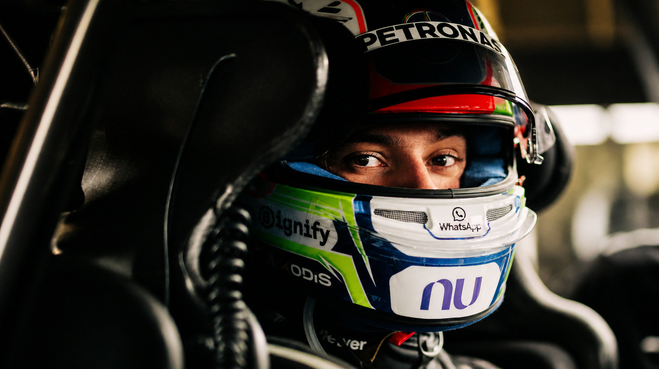 Piloto de Fórmula 1 com capacete colorido e expressão concentrada dentro do carro de corrida.