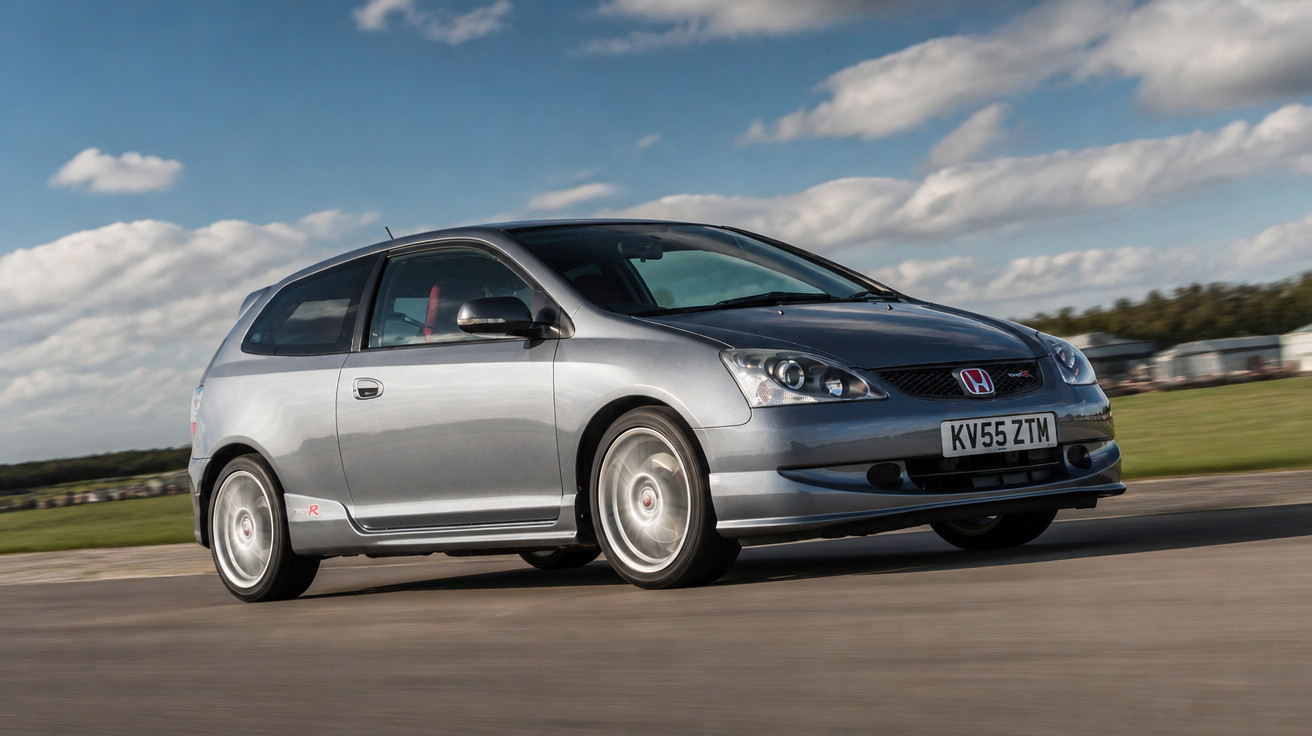 Carro esportivo prata Honda Civic Type R em movimento rápido em pista sob céu com nuvens.