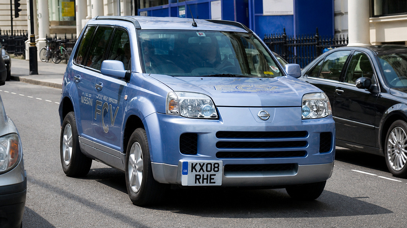 Carro SUV azul da Nissan estacionado em rua urbana com placas britânicas e prédios ao fundo.