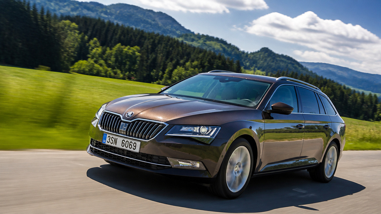 Carro perua marrom escuro da marca Skoda em estrada com natureza e montanhas ao fundo.
