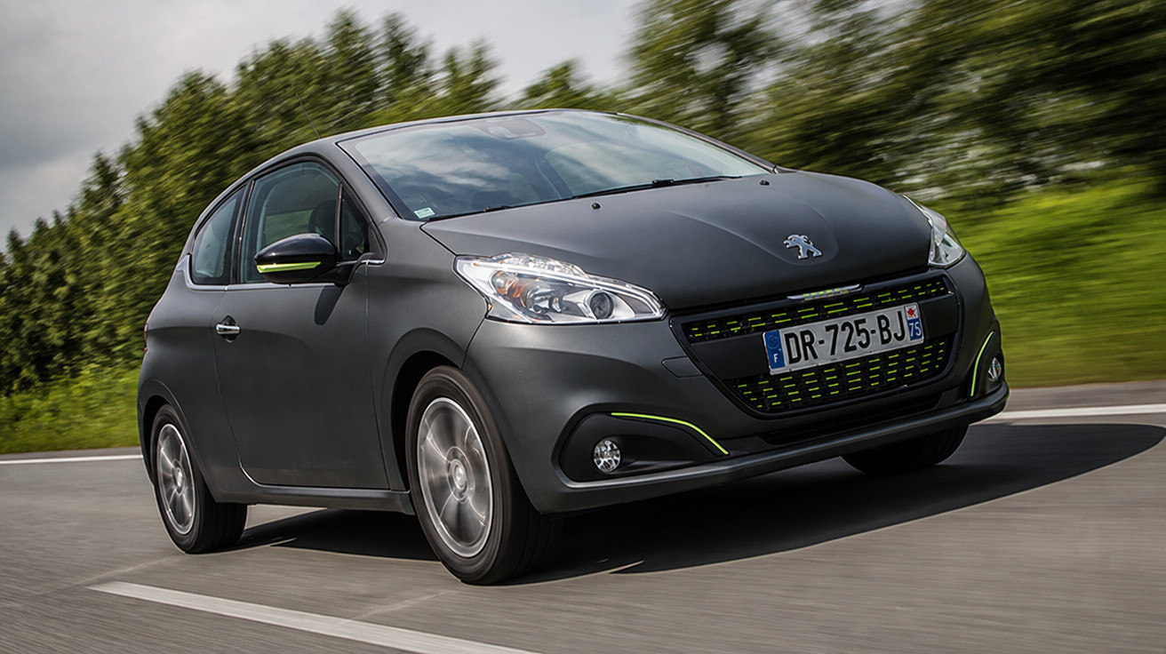 Carro Peugeot cinza escuro em movimento em estrada com árvores ao fundo em dia nublado.
