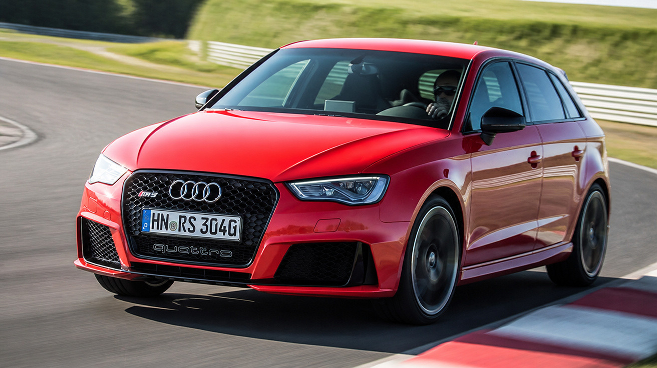 Carro vermelho Audi RS3 Sportback em alta velocidade em pista de corrida, com motorista usando óculos escuros.