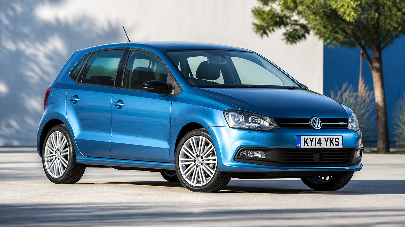 Carro hatchback Volkswagen azul estacionado ao ar livre com árvores ao fundo.