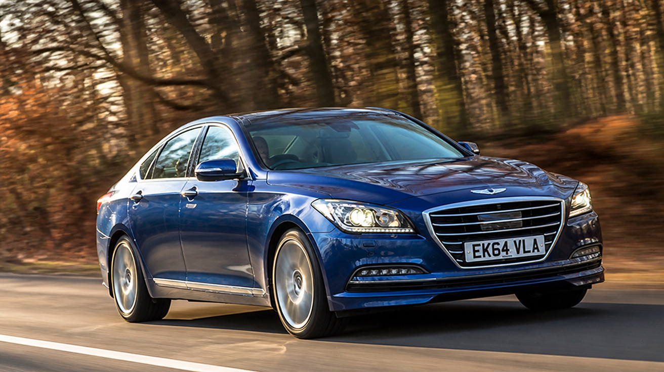 Carro sedã azul em movimento em estrada cercada por árvores com folhas secas.