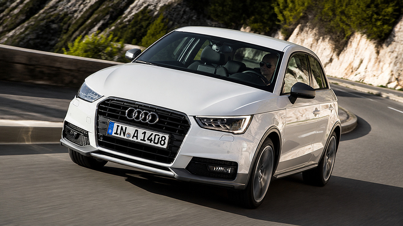 Carro Audi branco dirigindo em estrada sinuosa com vegetação e pedras ao redor.