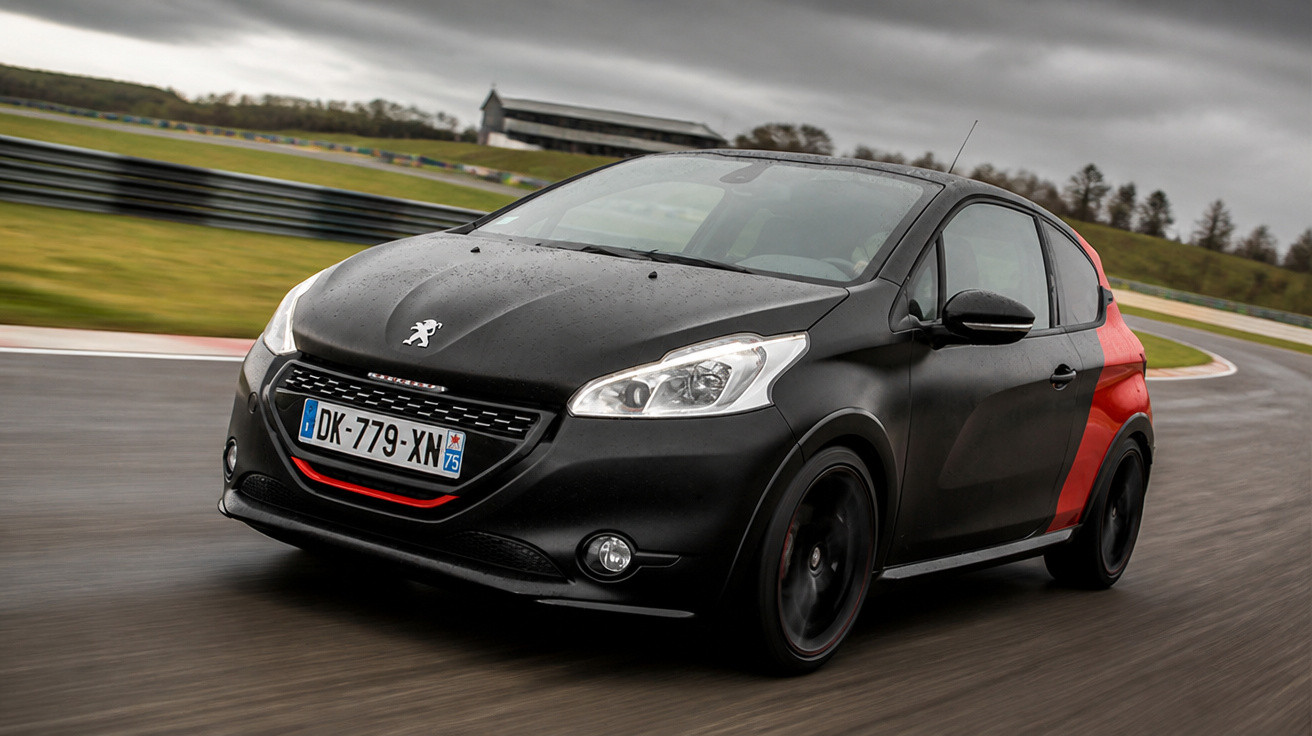 Peugeot preto com detalhes em vermelho em pista de corrida sob céu nublado, em curva de alta velocidade.