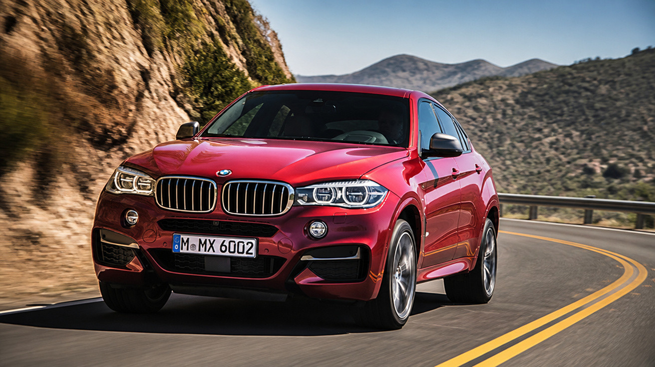 Carro SUV BMW vermelho em estrada sinuosa com montanhas ao fundo em dia ensolarado.