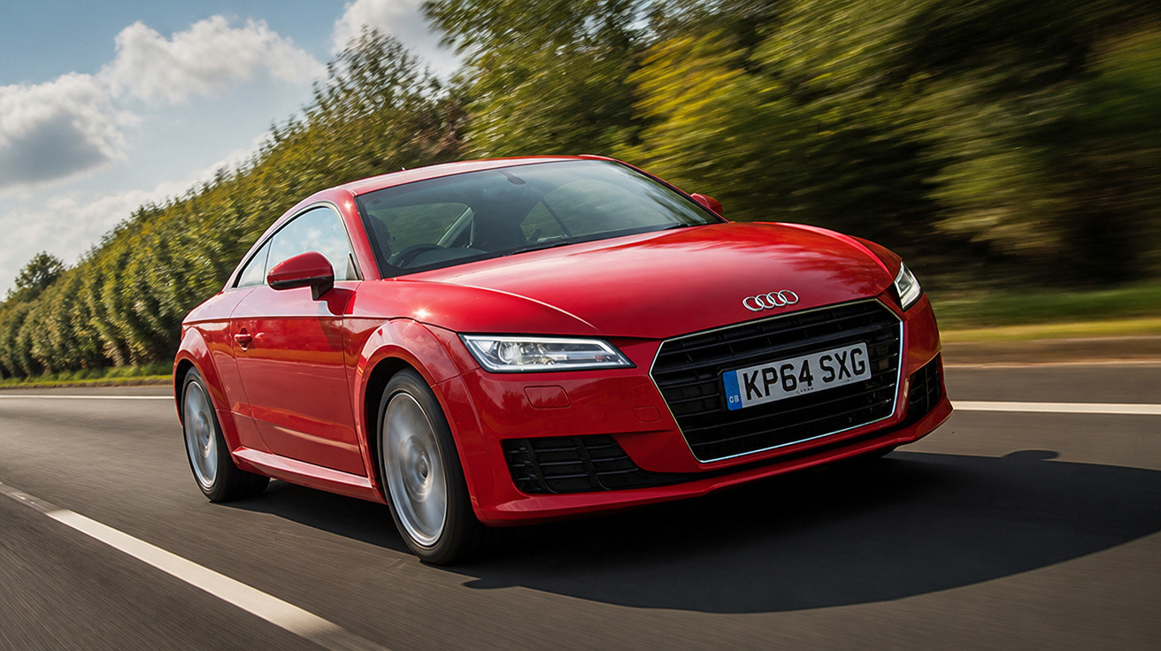 Carro esportivo vermelho Audi trafegando em estrada cercada por árvores sob céu parcialmente nublado.