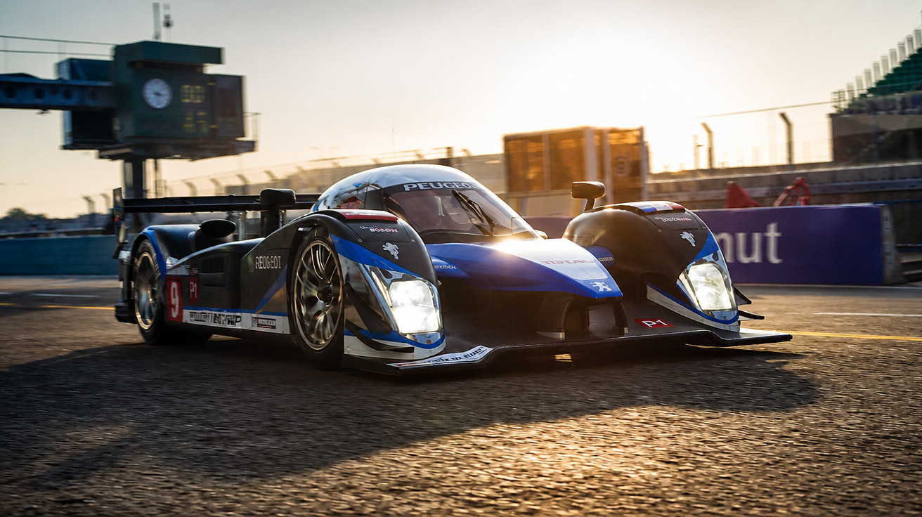 Carro de corrida Peugeot P1 azul e preto na pista durante o pôr do sol em competição.
