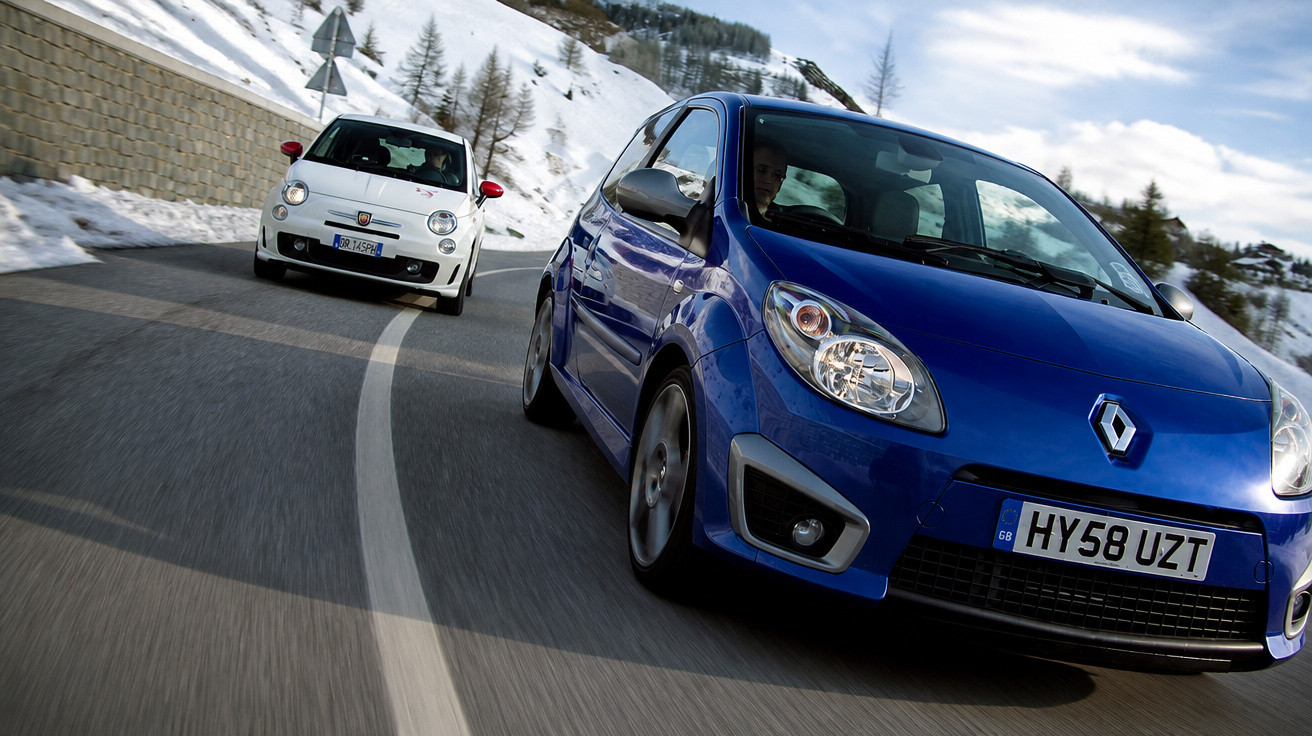 Carros azul Renault e branco Fiat circulando em estrada de montanha com neve ao redor.