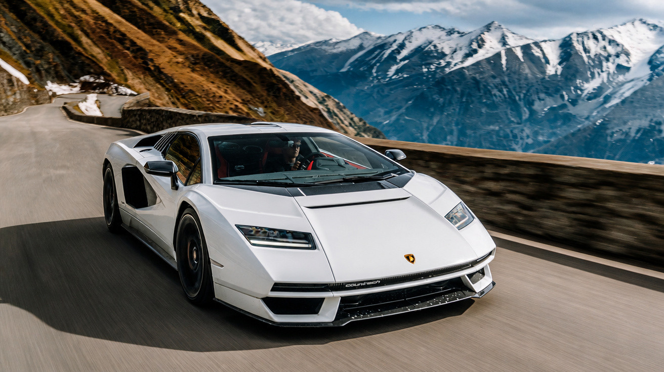 Carro esportivo branco dirigindo em estrada de montanha com picos nevados ao fundo.