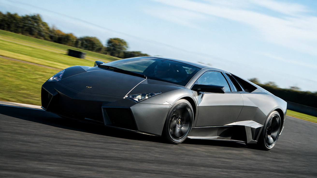 Carro esportivo preto de alta performance acelerando em pista de corrida sob céu azul.
