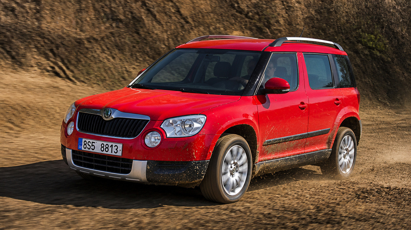 Carro SUV vermelho da marca Škoda trafegando em estrada de terra com poeira ao redor.