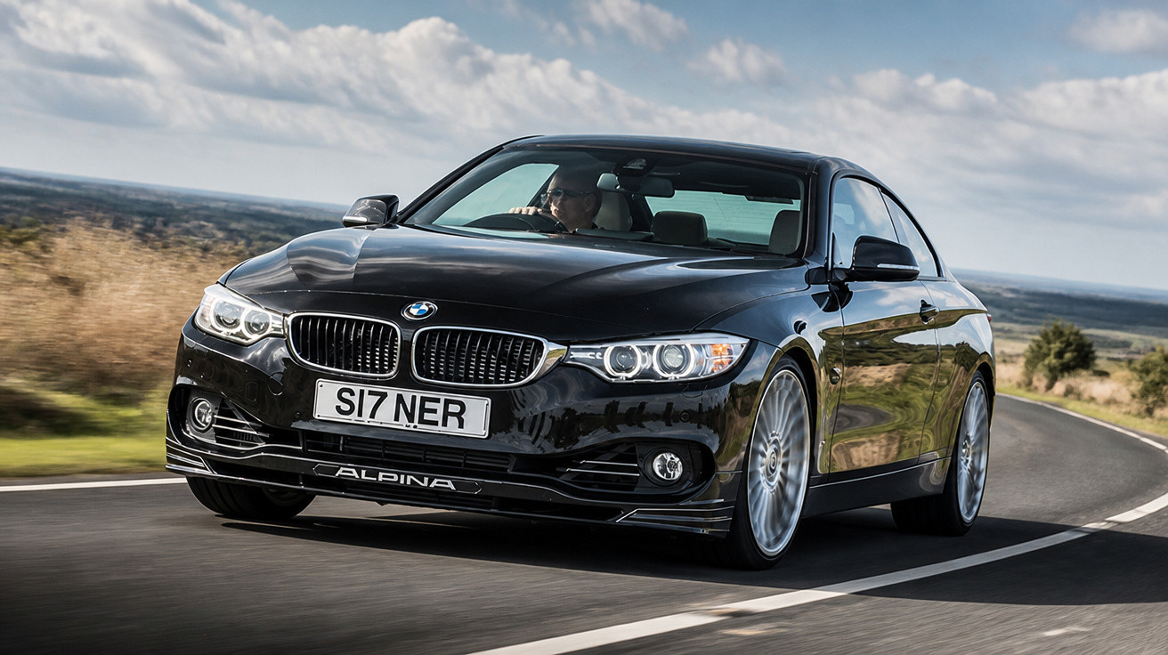 Carro preto BMW Alpina em estrada sinuosa sob céu parcialmente nublado, em movimento.