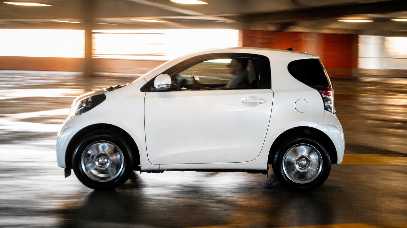 Carro branco compacto em movimento dentro de estacionamento com luz ambiente amarela e paredes de concreto.