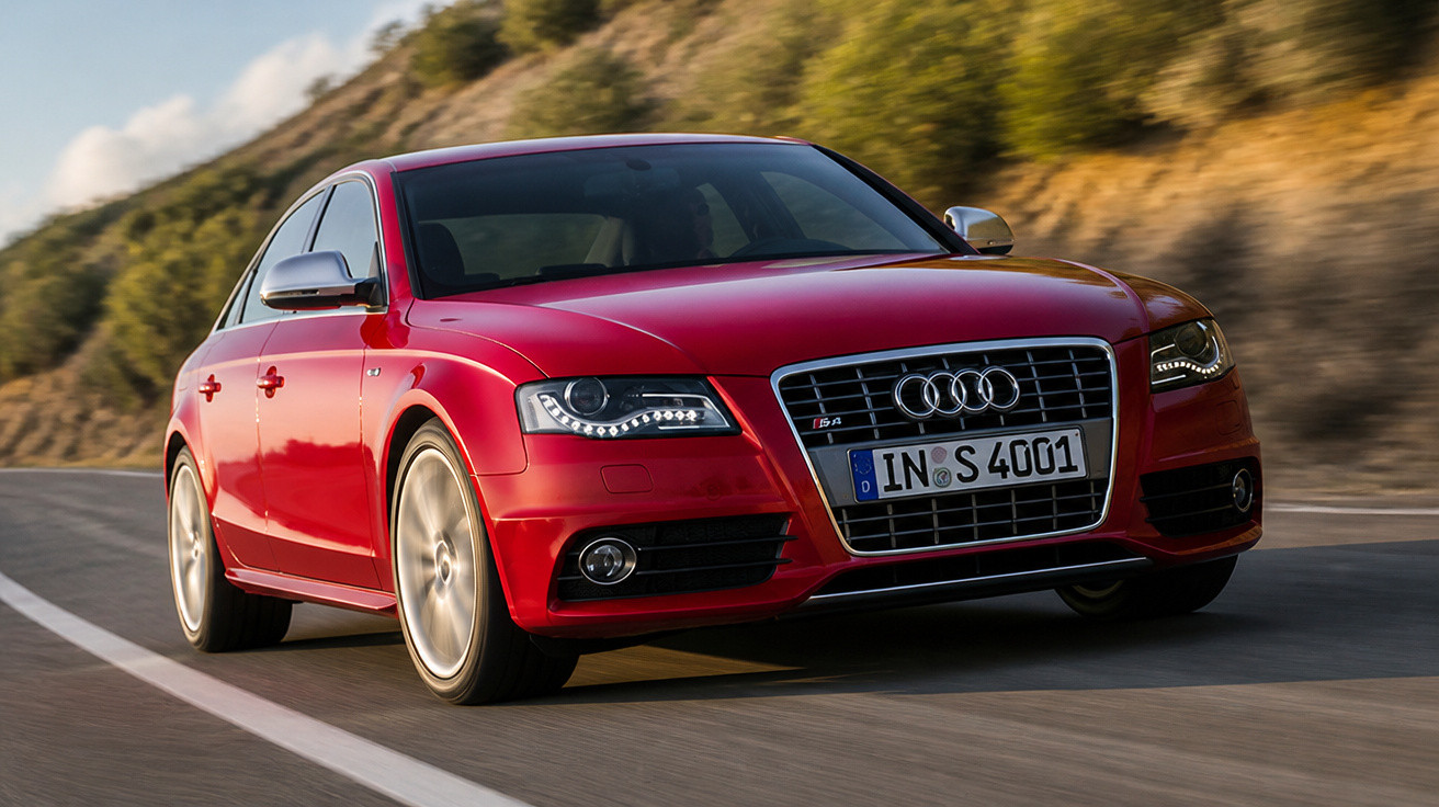 Carro Audi vermelho em movimento em estrada sinuosa com paisagem verde ao fundo.