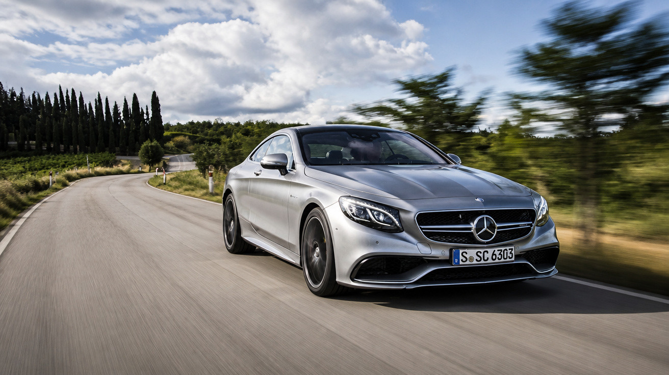 Carro esportivo prata Mercedes-Benz S Coupé trafegando em estrada sinuosa cercada por árvores e céu nublado.