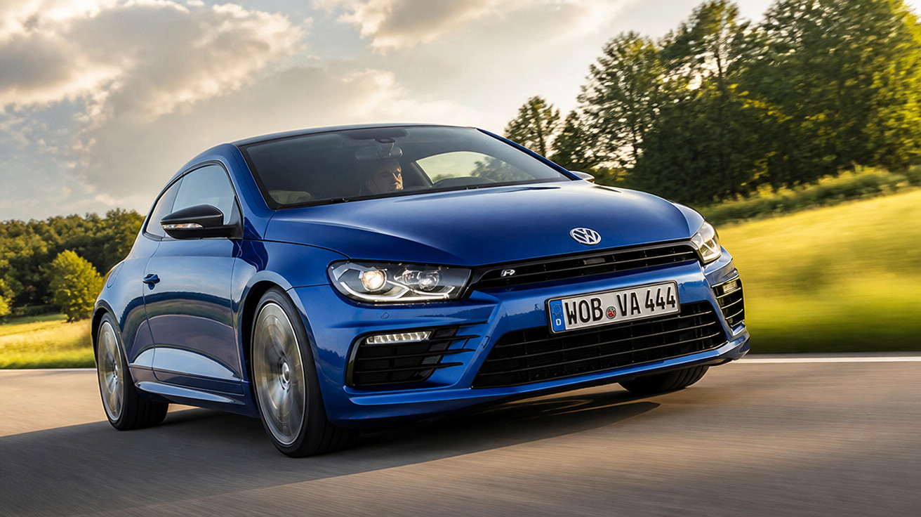 Carro esportivo Volkswagen azul em movimento em estrada cercada por árvores e gramado sob céu com nuvens.