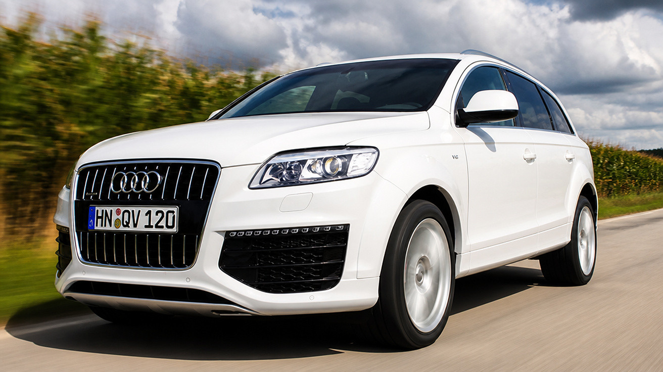 Carro SUV Audi branco em movimento em estrada com céu nublado ao fundo.