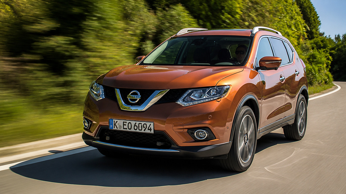SUV Nissan X-Trail laranja dirigindo em estrada curva cercada por árvores verdes