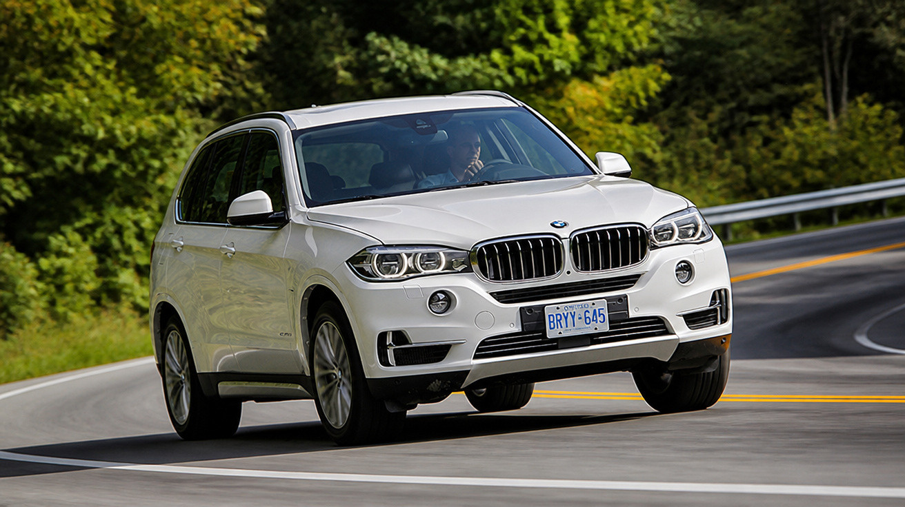 Carro SUV branco da BMW em curva de estrada rodeada por árvores verdes em dia ensolarado.
