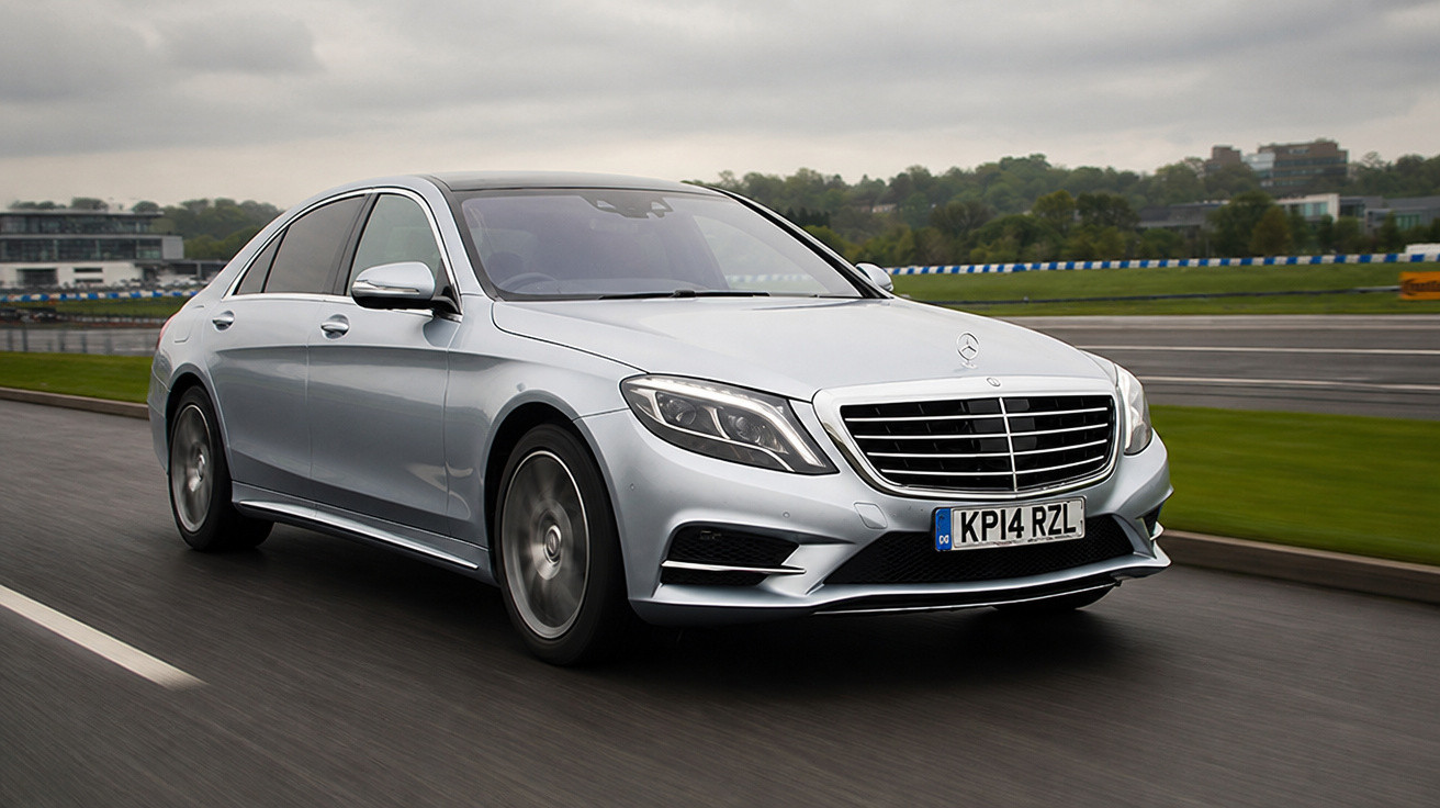 Carro Mercedes-Benz prata em movimento em pista de corrida sob céu nublado.
