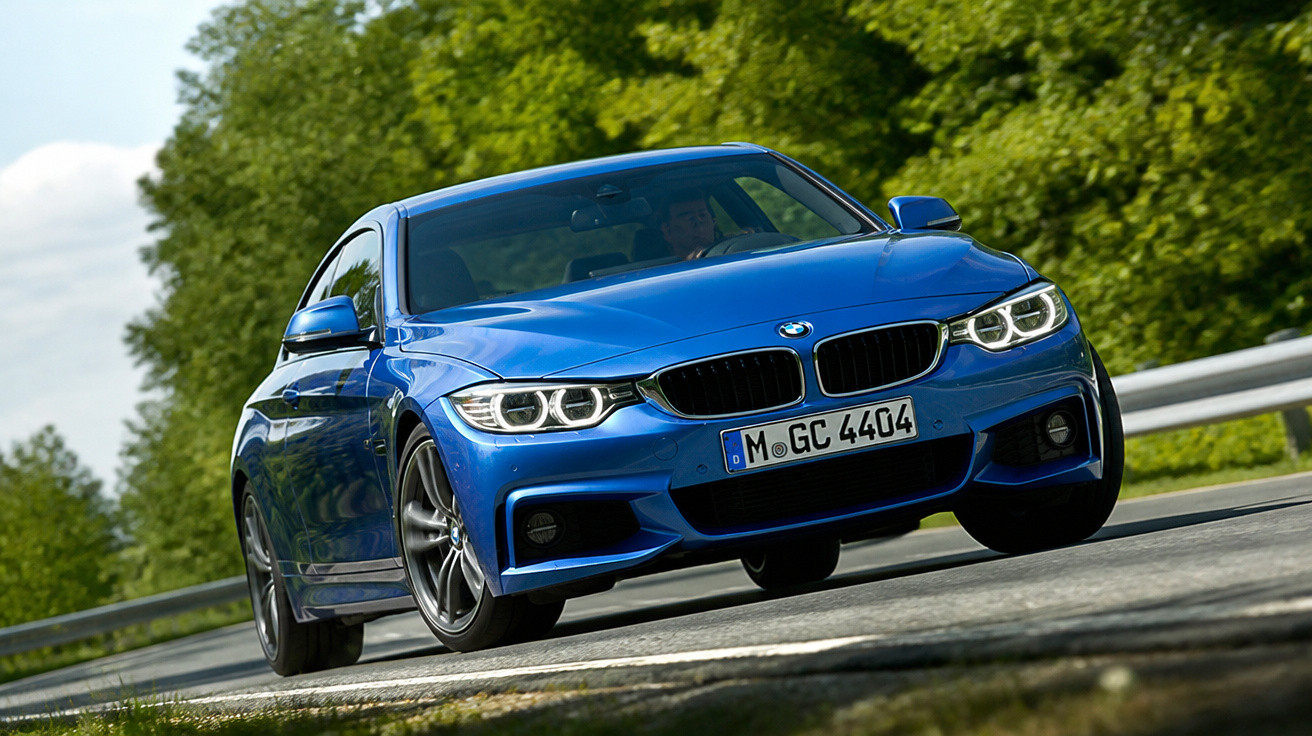 Carro azul BMW em movimento em estrada com vegetação ao fundo em dia ensolarado.