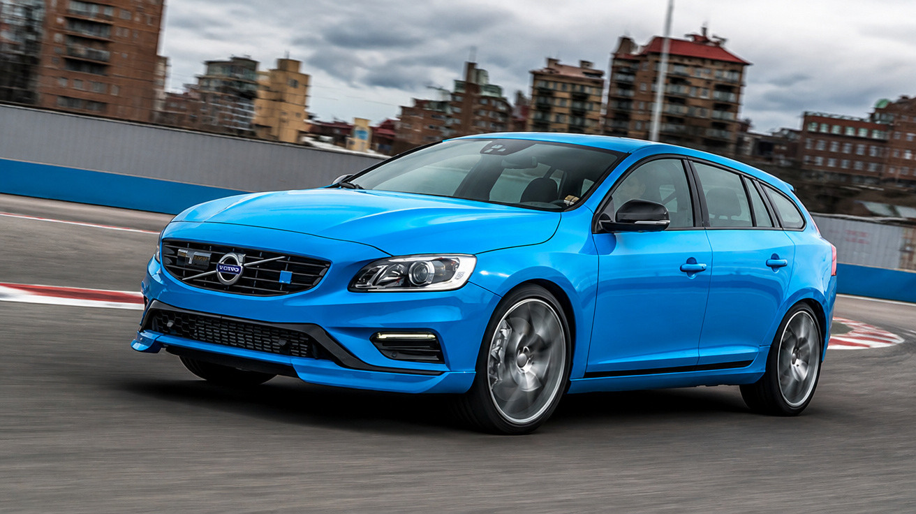 Carro azul Volvo em pista de corrida com prédios ao fundo em dia nublado.