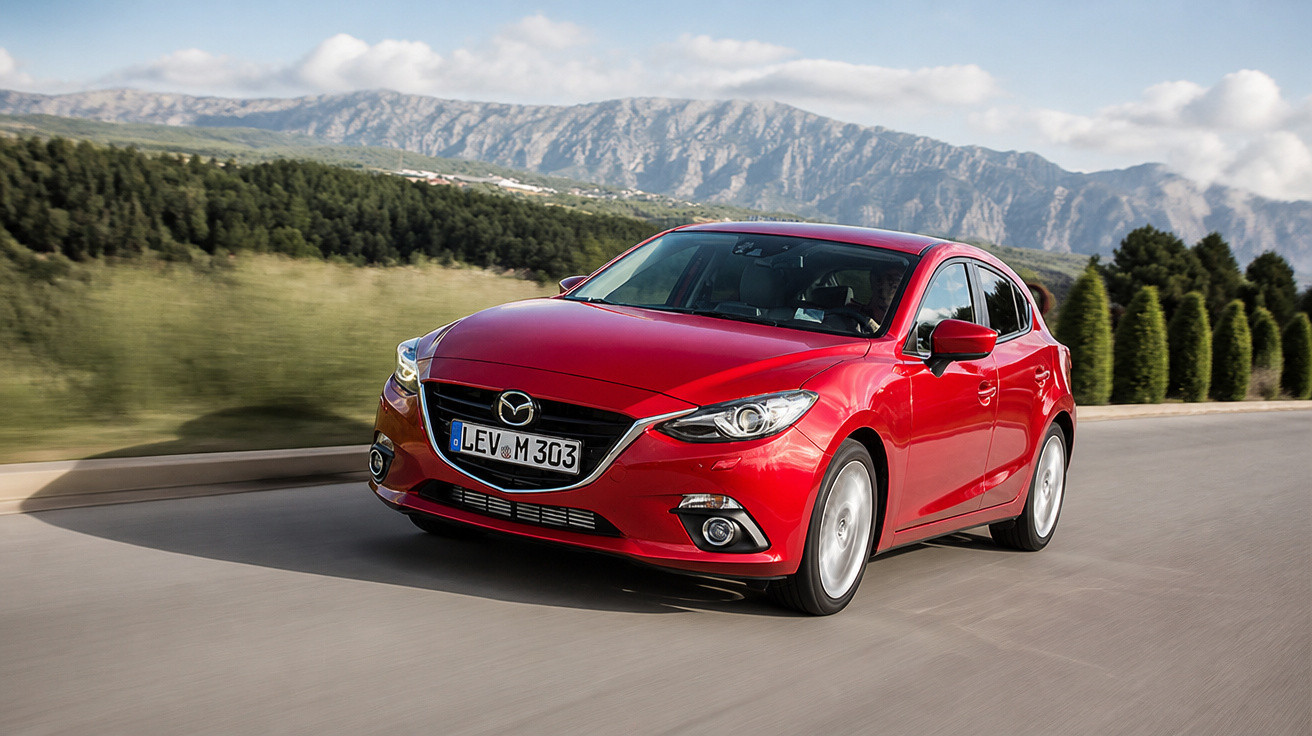 Carro vermelho Mazda 3 em movimento na estrada com montanhas ao fundo em dia ensolarado