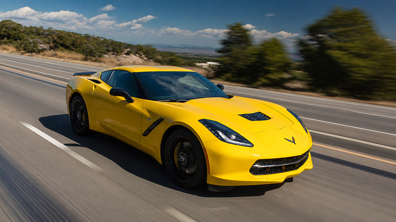 Carro esportivo amarelo em alta velocidade em estrada com paisagem natural ao fundo.