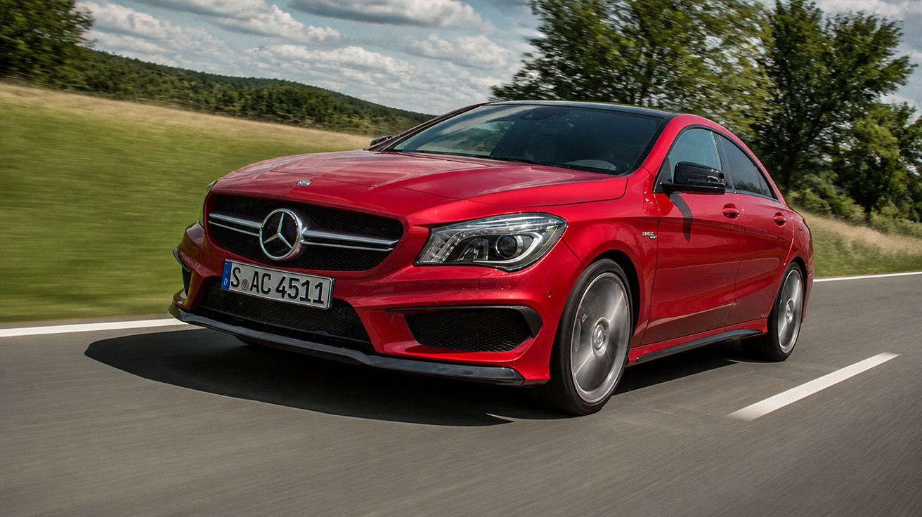 Carro Mercedes-Benz vermelho em movimento em estrada com paisagem e céu nublado ao fundo.