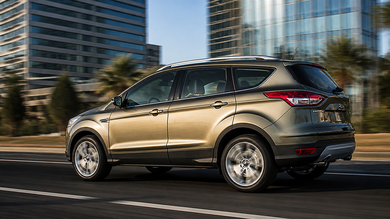 Carro SUV dourado em movimento em uma avenida urbana com prédios ao fundo.