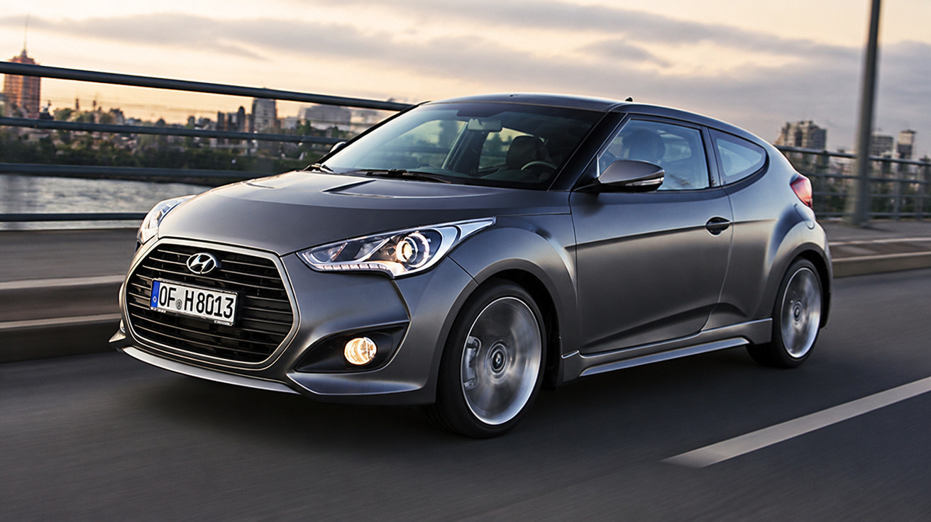 Carro Hyundai cinza em movimento em uma estrada urbana ao entardecer.