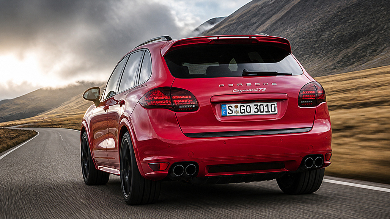 SUV vermelho Porsche Cayenne GTS em estrada com montanhas ao fundo sob céu nublado.