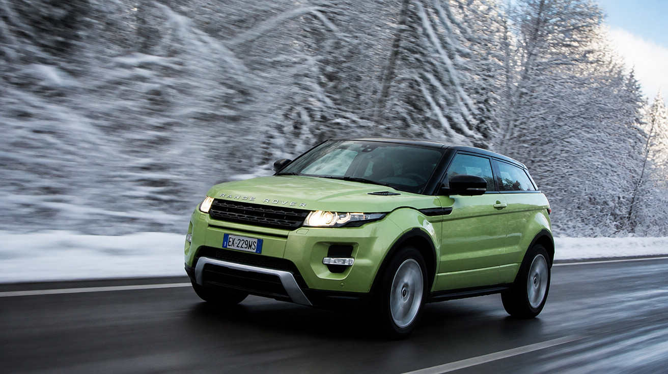 Carro verde Range Rover Evoque trafegando em estrada molhada cercada por árvores cobertas de neve.