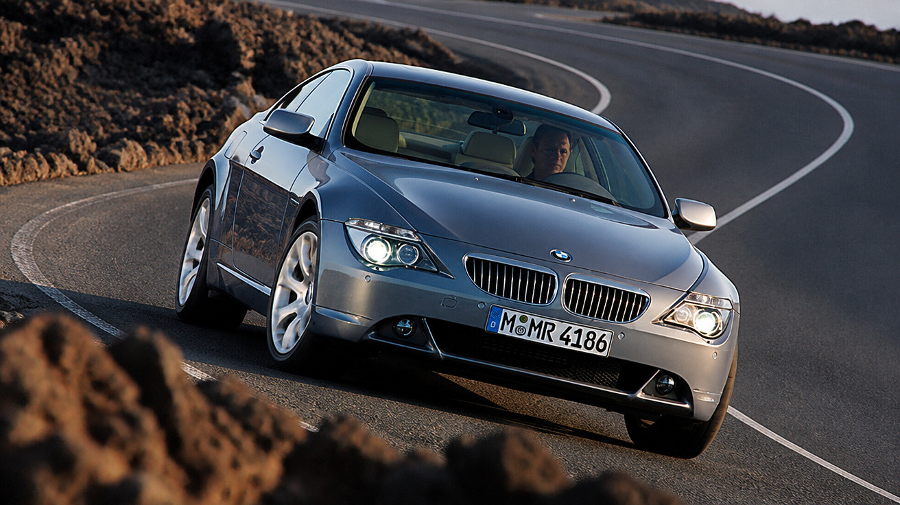 Carro BMW prata em curva de estrada sinuosa com motorista visível ao volante.