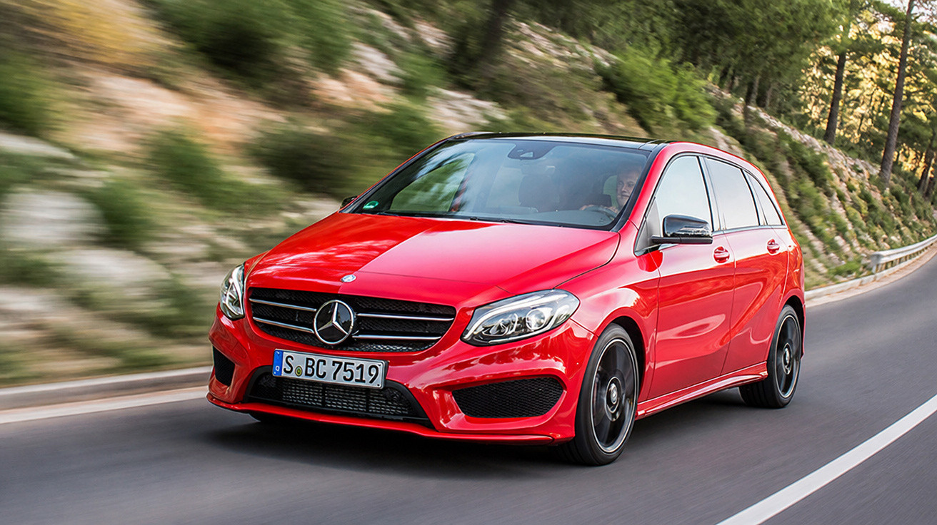 Carro Mercedes-Benz hatchback vermelho circulando em estrada sinuosa cercada por vegetação.