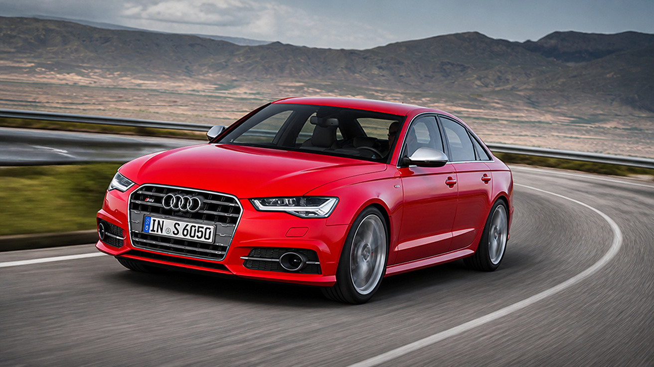 Carro sedã esportivo vermelho Audi S6 em curva de estrada cercada por montanhas e céu nublado.