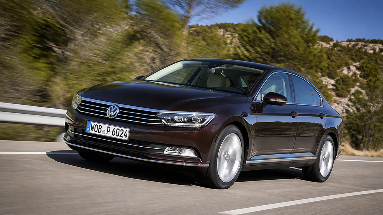 Carro sedan Volkswagen marrom em movimento em estrada asfaltada com árvores ao fundo.