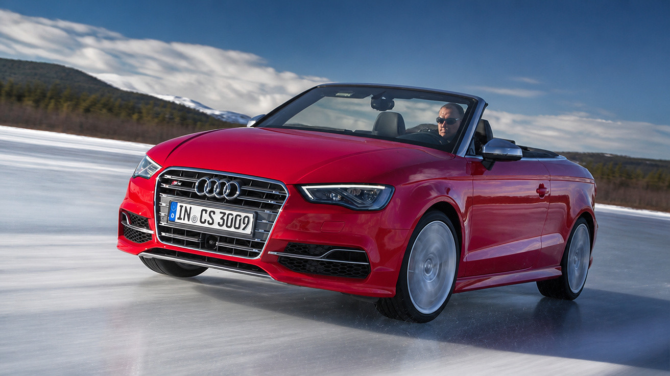 Carro conversível Audi vermelho dirigindo em superfície congelada com homem ao volante e céu nublado.