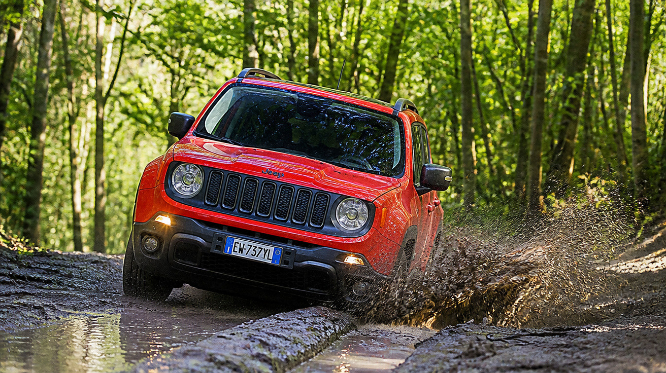 Carro Jeep vermelho atravessando lama em estrada de terra cercada por árvores verdes.