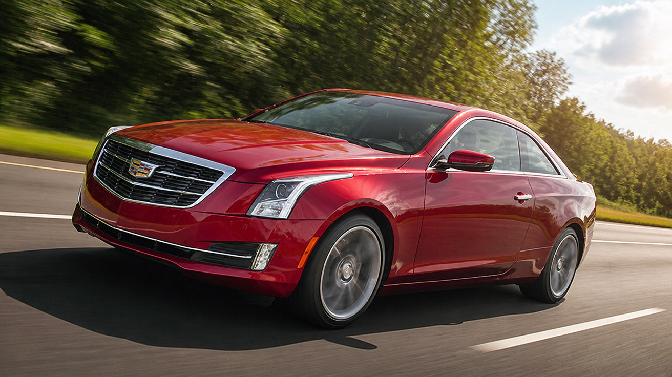 Carro vermelho Cadillac em alta velocidade na estrada com árvores ao fundo em dia ensolarado.