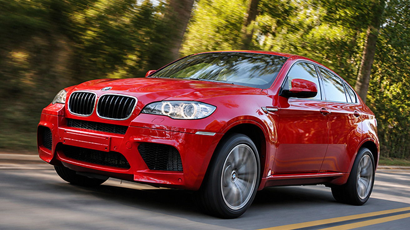 Carro SUV vermelho da BMW em alta velocidade em estrada cercada por árvores verdes.