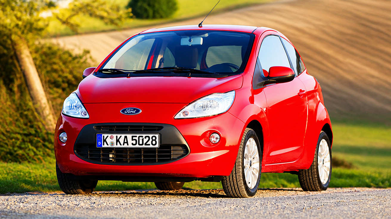 Carro Ford Ka vermelho estacionado em estrada de terra com fundo de campo e árvore.